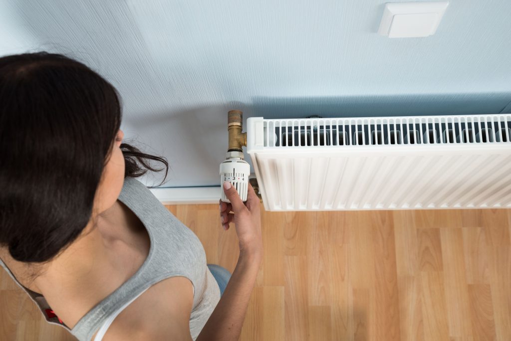 Young woman turning thermostat on radiator, High Angle View Of Woman Turning Thermostat On Radiator