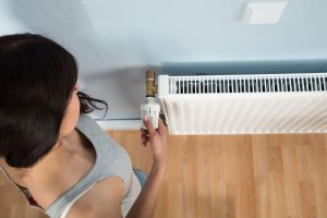 Young woman turning thermostat on radiator, High Angle View Of Woman Turning Thermostat On Radiator